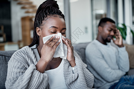 除了流感 我什么都可以和你分享 一个年轻的女人正在擤鼻涕 她的丈夫坐在她旁边的沙发上图片