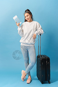 穿着休闲服准备带着行李和门票在蓝色背景下旅行的快乐女性的全长图像乘客游客护照女孩手提箱假期图片