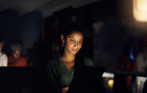 选择快速高效的方式来完成工作 一个年轻的女商务人士晚上在办公室里使用数字平板电脑图片