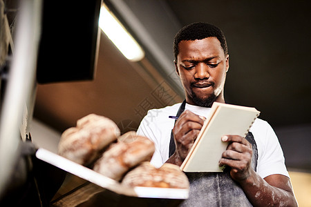 一位男性面包师在面包店工作时做笔记的 我当时正在准备我的订货单图片