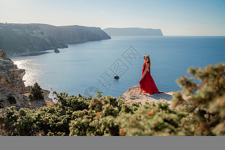 一个穿着红色飞行服的女人 在大海的背景下 飘在风中发抖着旅行女性飞行女孩魅力女士衣服尾巴自由天空图片
