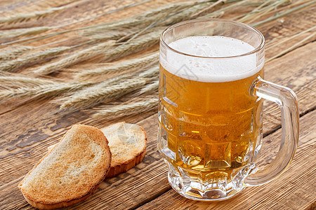 一杯啤酒 有大麦耳朵和木本底的面包啤酒厂气泡饮料木头金子液体发泡白色桌子玻璃图片