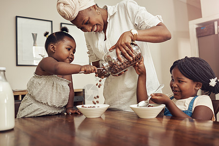 一位年轻母亲在家为两个可爱的年轻女儿准备麦片 她想请妈妈多加一点图片