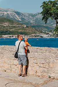 可爱的家庭在海滩上玩得很开心 父亲和孩子在蔚蓝的大海和天空的映衬下 旅行 积极的生活方式 假期 休息的概念 一个男人带着孩子在岸图片