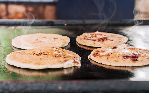 传统的烤奶酪 pupusas 烤架上四个传统手工制作的 pupusas 的特写 传统的尼加拉瓜 pupusas 烤架上有融化的奶图片