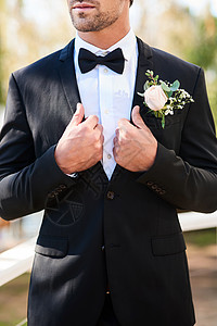 他喜结良缘 一个面目全非的年轻新郎调整他的西装 并在他的婚礼当天在户外做准备背景图片