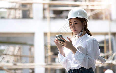 有蓝图的建筑师在建筑工地 身穿白色头盔和安全黄色背心的女建设者画像 心烦意乱 怀疑 严肃的女人在户外看着手机屏幕科学说话财产女孩图片