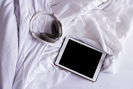 一个平板电脑和耳机 躺在折叠的白色白床上 顶端视图 特写图片