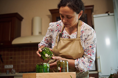 有魅力的家庭主妇煮自制泡菜 用瓜子罐头 倒在厨房的木纸箱上图片