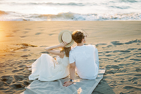 戴帽子的女人坐在沙滩的毯子上 靠着一个男人肩膀图片