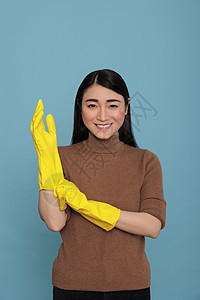 微笑着高兴而高兴的亚洲女佣将黄色橡胶手套放在手边图片