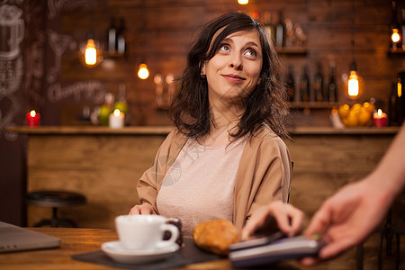 美女在咖啡店里抬头看着咖啡师 用现代支付方式支付咖啡的画像图片