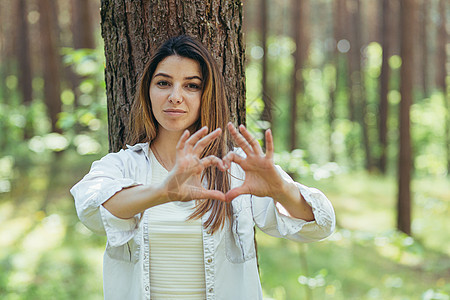 年轻美女志愿者在树旁的树林里做志愿者 微笑着看着镜头 用手和手指展示一颗心 这是热爱大自然的标志自由环境叶子幸福情感生态日落森林图片