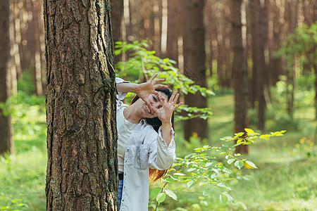 年轻美女志愿者在树旁的树林里做志愿者 微笑着看着镜头 用手和手指展示一颗心 这是热爱大自然的标志情感手势环境女孩喜悦日落森林季节图片
