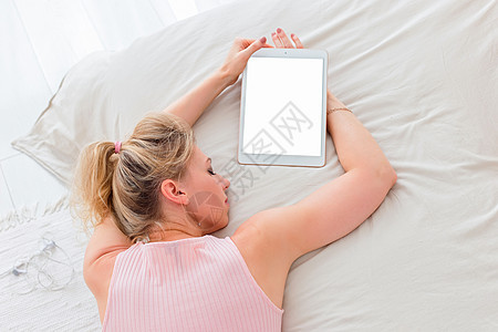 金发瘦弱的苗头女人 清晨粉红色顶部躺在白床上 带数字平板电脑图片