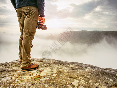 摄影师在山悬悬悬崖上寻找雾 Hiker将拍摄照片记录顶峰远足探索蓝色记者邮差岩石男人职业图片