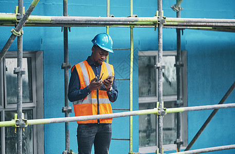 男性建筑工人在手机上检查数字建筑计划 忙碌的城市发展建设者查看建筑规划数据 通过双向无线电提供行业信息图片