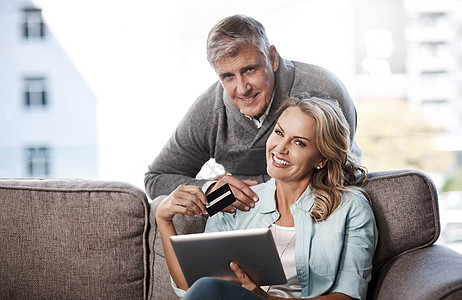 我们可以在线访问一些最优惠的价格 一对成熟夫妇在家使用数字平板电脑和信用卡进行在线购物的肖像图片