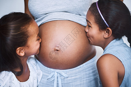 可爱过头 白天在家里 两个快乐的小女孩站在妈妈身边亲吻她怀孕的肚子图片