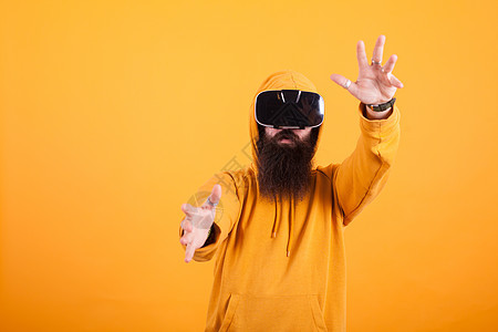 有吸引力的长胡子长胡子的年轻男子 身着虚拟现实头盔 在黄色背景上手势图片