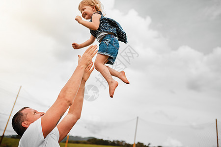 她喜欢和爸爸在一起的时光 一个成熟的男人把他年幼的女儿扔到空中 然后在外面接住她背景图片