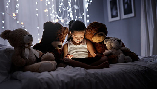 别让深夜的屏幕时间变成一种不健康的习惯 一个可爱的小女孩晚上在床上用数字平板电脑图片