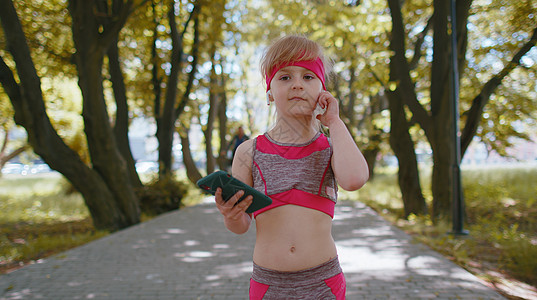 运动健身运动跑步女童行走 使用带耳机的智能手机听音乐公园有氧运动动机体操女性学校活动活力保健行动图片