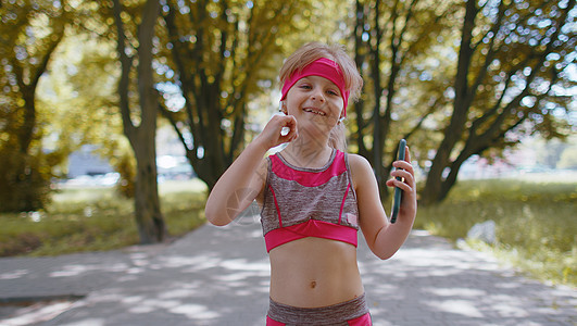 运动健身运动跑步女童行走 使用带耳机的智能手机听音乐活力女性放松运动员有氧运动爱好运动装活动休息孩子们图片