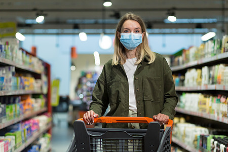 身戴医疗面罩的妇女在超市推推车零售购物者消费者预防产品顾客面具市场疾病女士背景图片