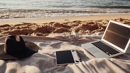 海边Sandy海滩的Plaid Plaid上的笔记本电脑 板板和帽子近视 自由概念 远程工作图片