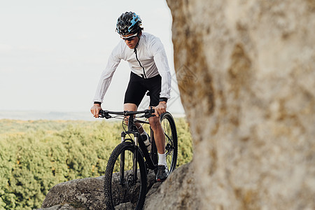 配备专业男性骑自行车的人骑山地自行车在岩石地形的小径上 成年男子享受他的极端爱好站在岩石上全景图片