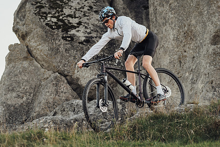 装备精良的职业自行车手骑着山地自行车下坡 运动员骑着自行车从山上下来 背景是巨石图片