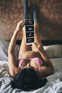 这些是许多人的第一张照片 一个迷人的年轻孕妇躺在家里的床上的全长镜头背景图片