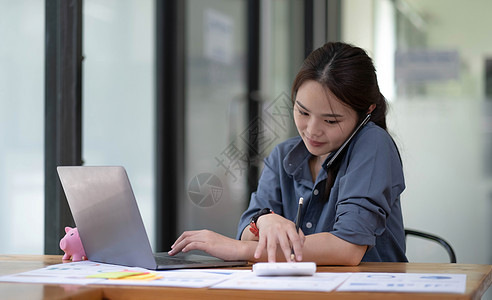 亚洲女经理在她的工作电脑上使用计算器记录数据时与商业客户通电话图片