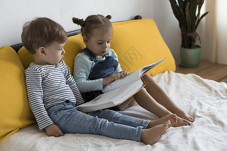 童话书两个学龄前儿童在黄色床上阅读一本有趣的童话故事书 小双胞胎读者的兄弟姐妹在家里隔离时玩得很开心 很开心 友谊 家庭 教育理念舞蹈背景