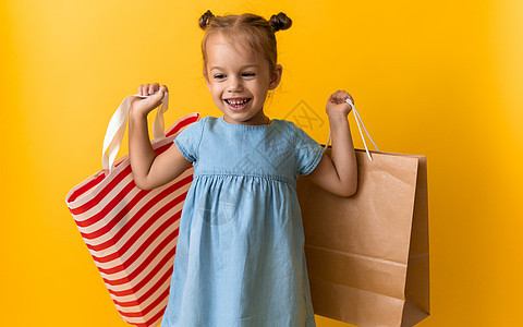 画像白种人美丽快乐的小学龄前女孩笑得开朗 拿着纸板袋 在橙黄色工作室背景下被隔离 幸福 消费主义 销售人员购物理念购物中心婴儿生图片