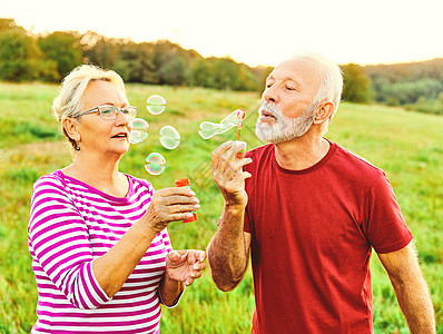 女人男人户外老年夫妇快乐乐趣退休一起泡泡肥皂吹爱老自然成熟背景图片