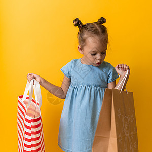 Squre 肖像白种人美丽快乐的学龄前小女孩开朗地笑着拿着纸板袋在橙黄色背景下被隔离 幸福 消费主义 销售人员购物理念图片