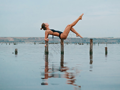 穿着泳装的年轻白人女性在水里曼 湖泊或河流中练习瑜伽 美丽的倒影 复杂的体式 平衡 健身 运动 瑜伽和健康的生活方式概念海洋沉思图片