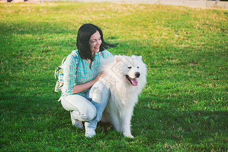 美丽的黑褐色女人与毛发白狗Samoyed 在公园绿草地上宠物孩子女性友谊女士朋友幸福快乐绿色女孩图片