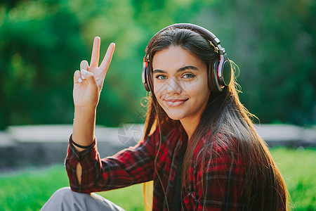 年轻的少年在公园里通过耳机听音乐 穿红色格子衬衫的女孩微笑着 随着节奏跳舞 学生生活 自由 现代青年的概念闲暇享受女性技术街道成图片