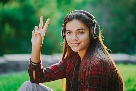 年轻的少年在公园里通过耳机听音乐 穿红色格子衬衫的女孩微笑着 随着节奏跳舞 学生生活 自由 现代青年的概念闲暇享受女性技术街道成图片
