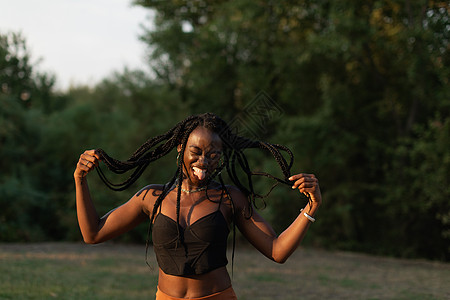 一位年轻黑人女性在公园里吐舌头时嬉戏地移动辫子的画像图片