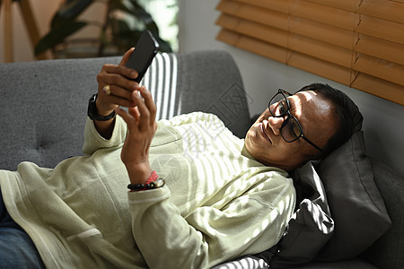 快乐的中年男子躺在家里的沙发上 用智能手机在社交网络上在线聊天图片