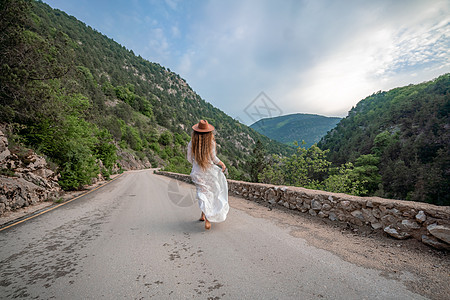 穿着棕帽子和白衣服的女性旅行者 看着令人惊叹的山峰和森林 漫游概念 大气史诗时刻假期女孩旅游自由山脉荒野旅行树木爬坡背包图片