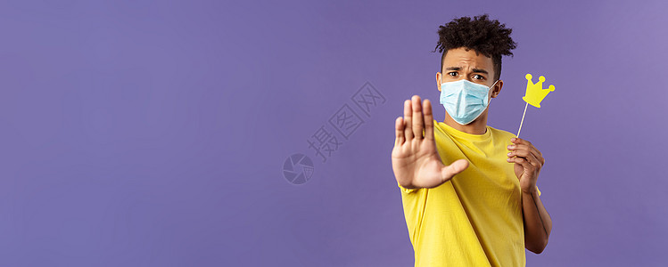 戴着医用面具的年轻嬉皮士特写肖像伸展手向前停止手势 拿着小纸冠 要求远离 保持 1 5 米距离 避免隔离期间的社会接触发烧流感流图片
