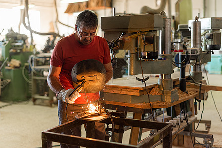 在一家制造厂焊接红色T恤衫的人图片