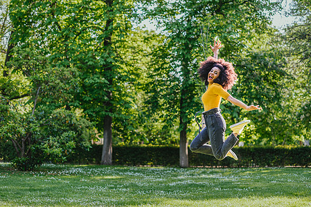 漂亮的女人在花园里快乐地跳了起来微笑享受卷发活力生活方式跳跃女孩女士动机喜悦图片