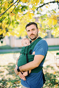 老爸抱着一个婴儿 在公园的树下站立背景图片