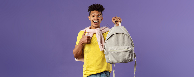 快乐的年轻英俊男学生的画像 男人推荐背包 背着背包 竖起大拇指 为大学学期买了新设备 紫色背景微笑培训班成人投资理发工作男朋友笔图片